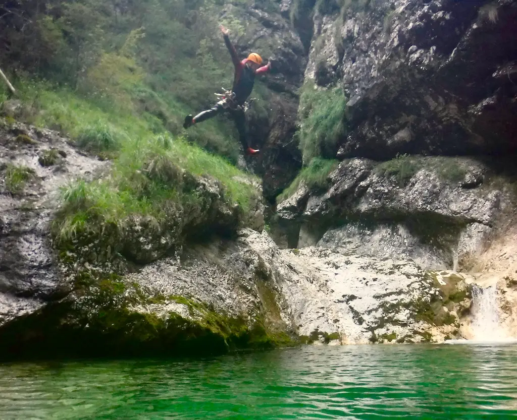 Canyoning Tour Teilnehmer spring mit ausgestreckten Armen in ein Wasserbecken währen einer Tour im Friaul